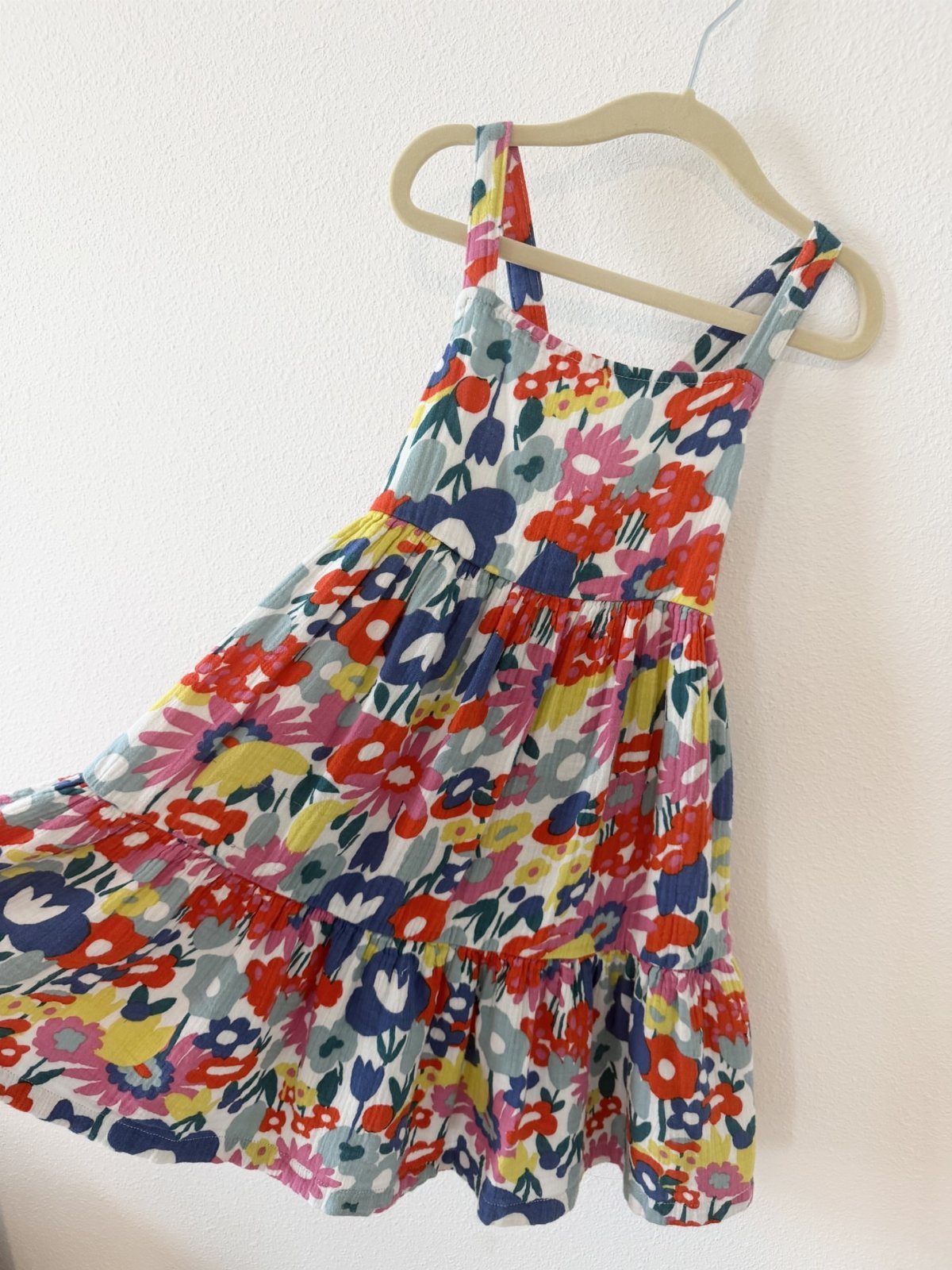 Floral print infant dress hanging on a beige hanger against a white wall