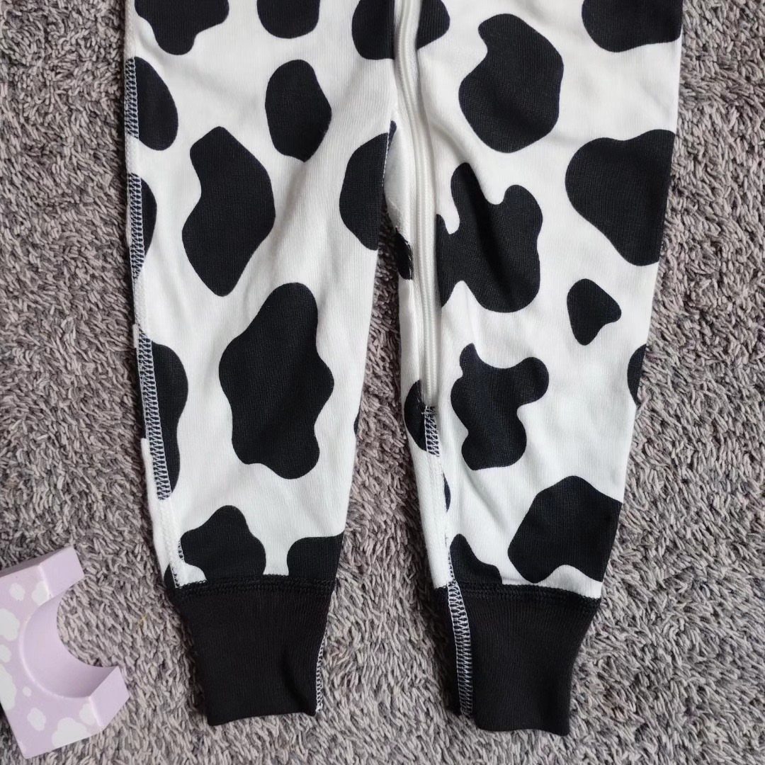 Cow-print infant pants with black cuffs on a grey textured carpet.