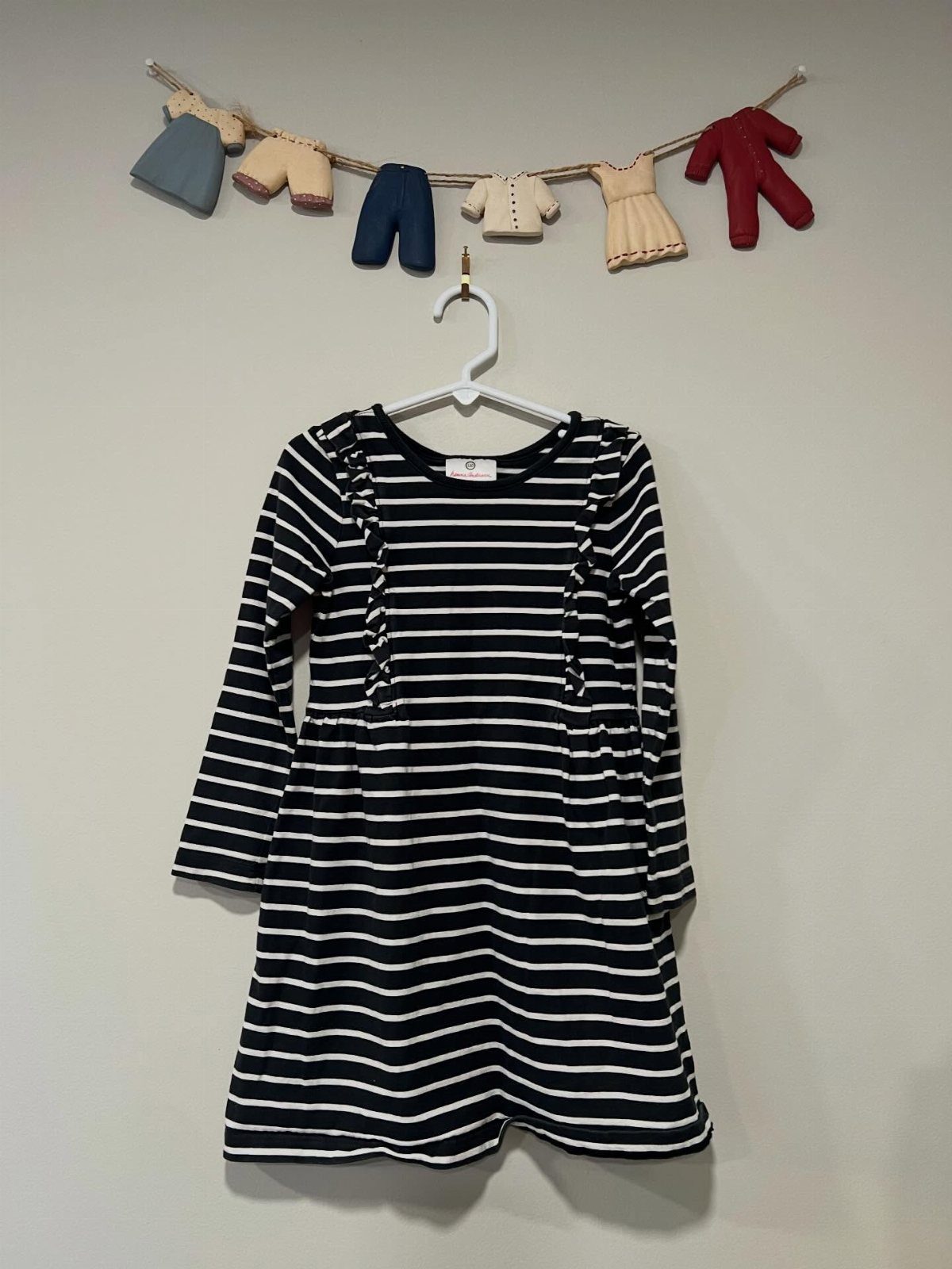 Striped navy and white infant dress hanging on a white plastic hanger.
