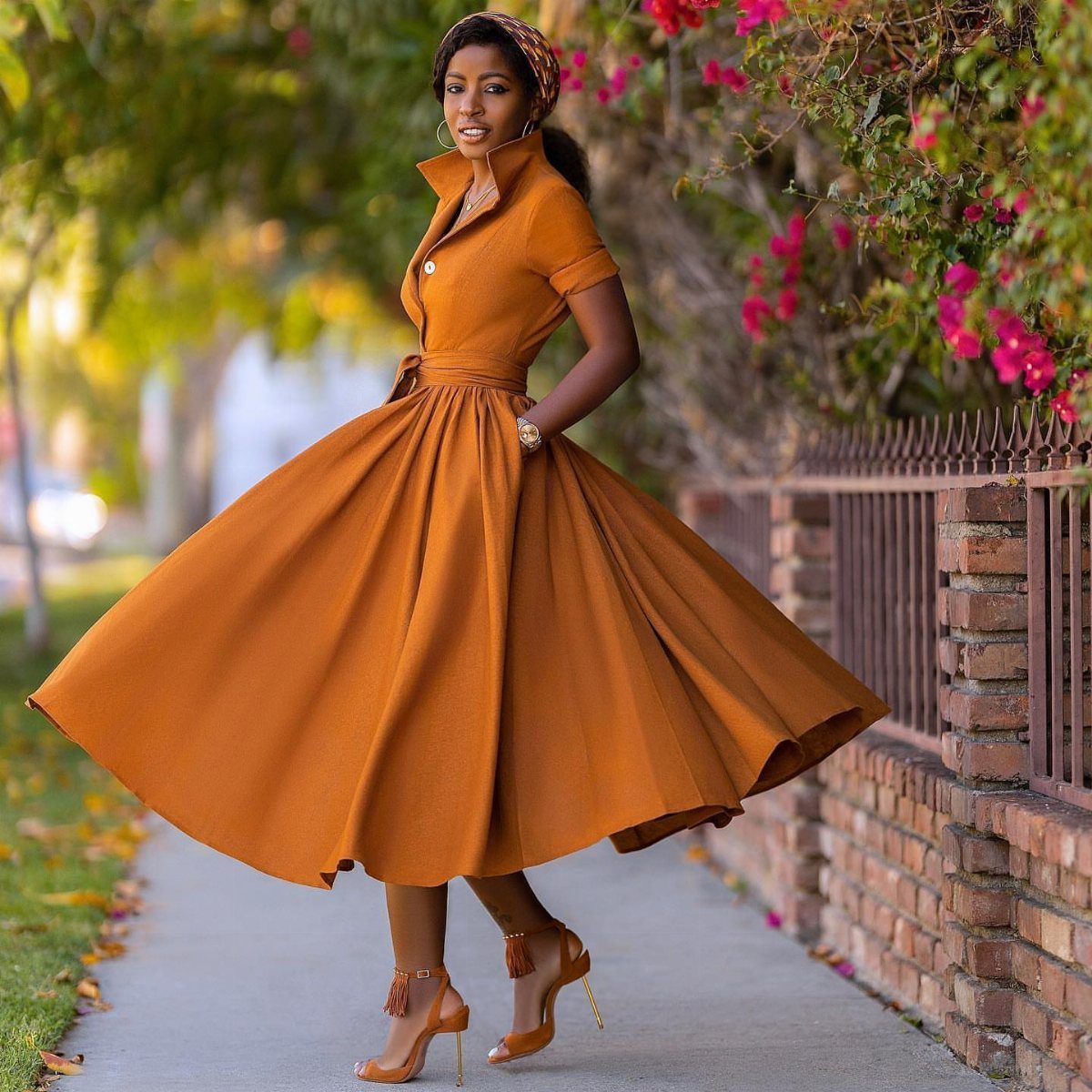 Woman in a burnt orange full-skirted dress and matching headwrap posing outdoors.
