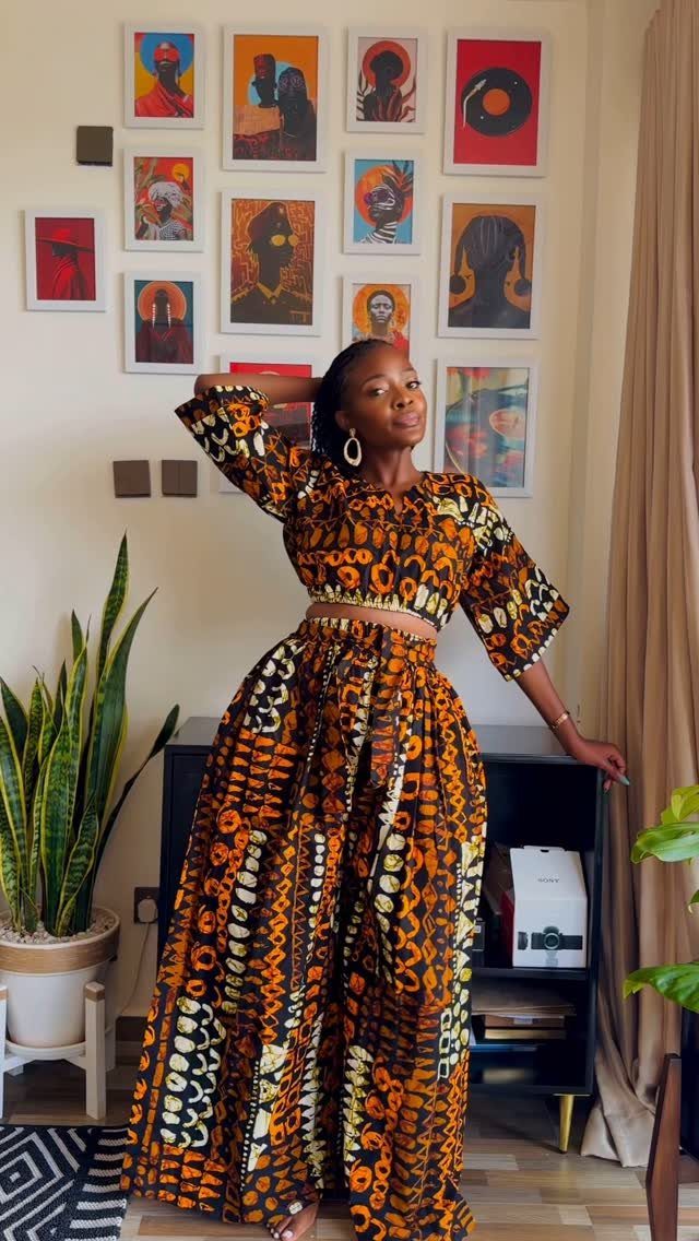 Woman wearing an orange and black African print crop top and wide-leg trousers.