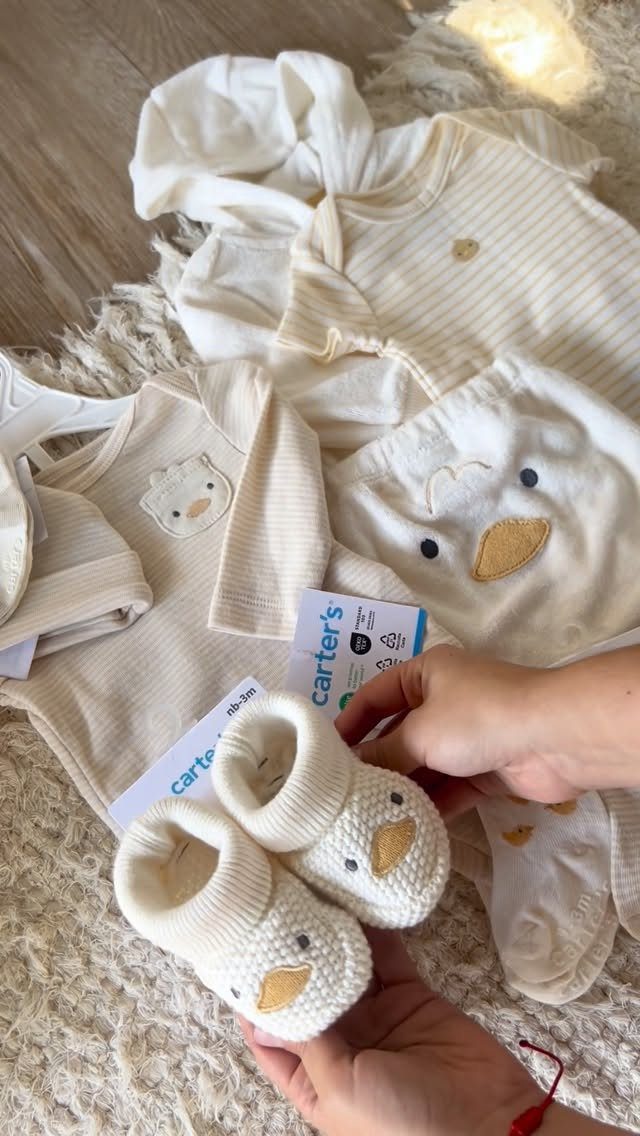 Cream baby booties and matching newborn clothes with Carter's tags on a rug