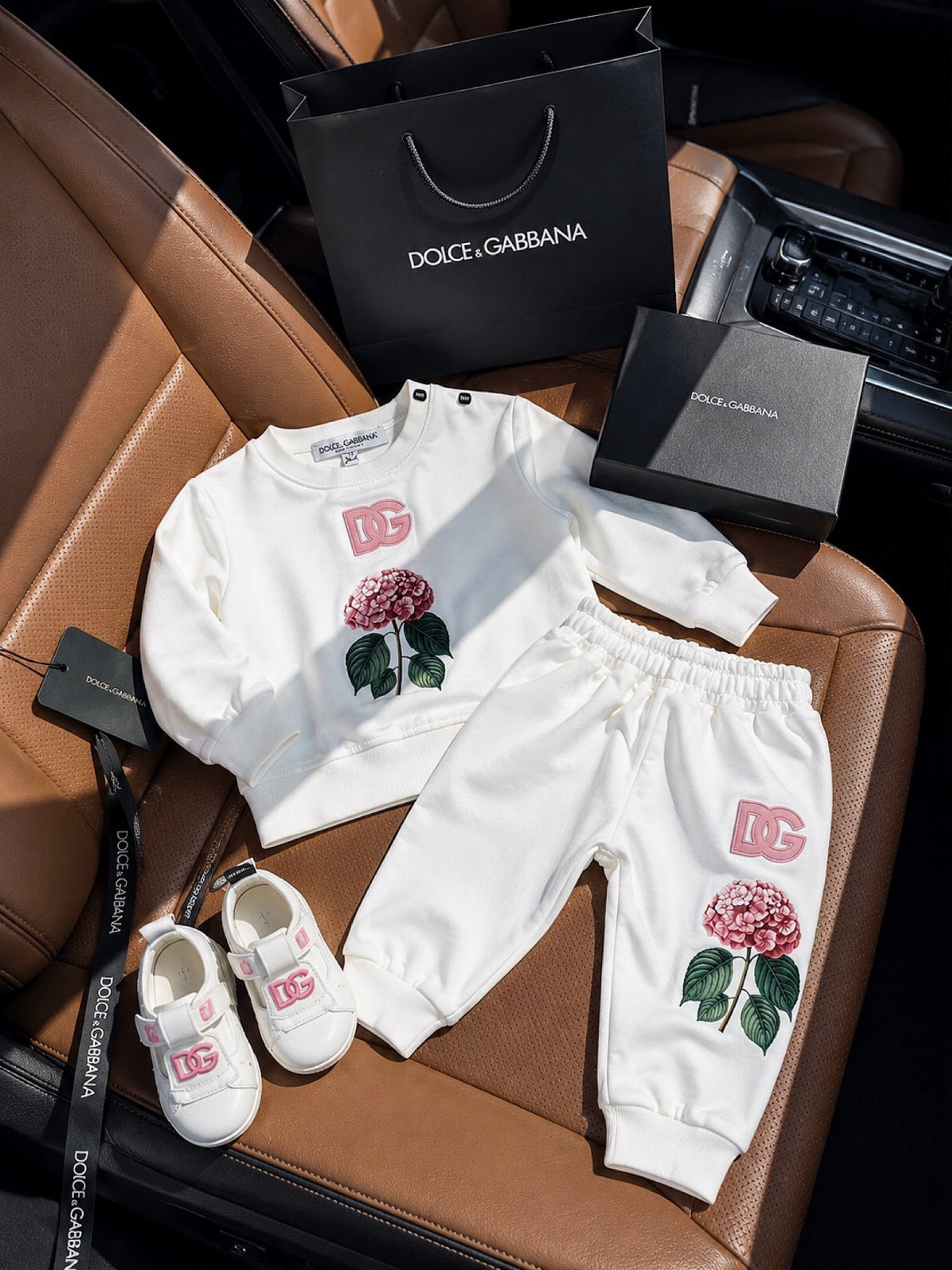 White Dolce & Gabbana newborn outfit with pink flower embroidery on brown leather seat