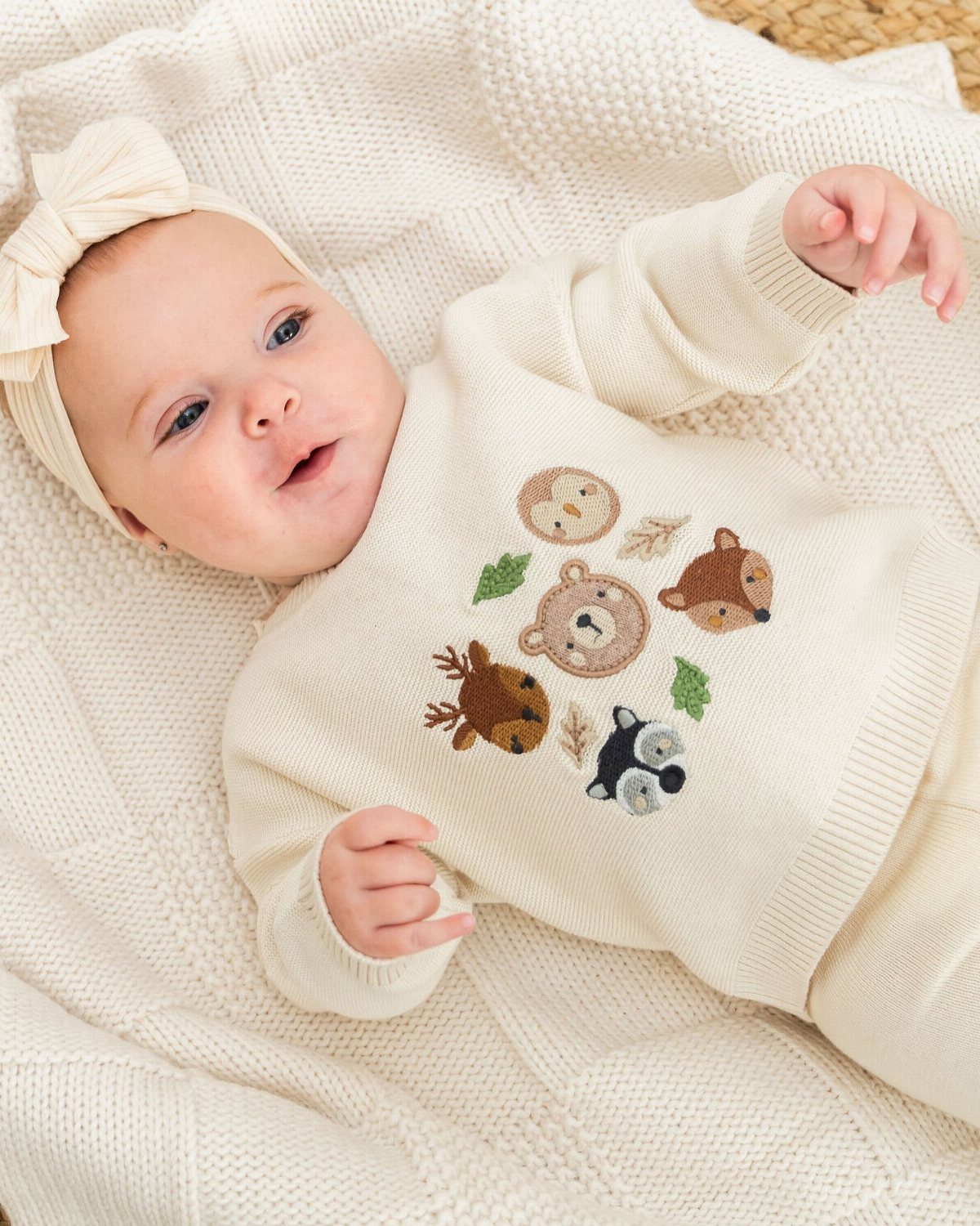 Newborn baby in a cream knitted sweater with animal embroidery on a white blanket