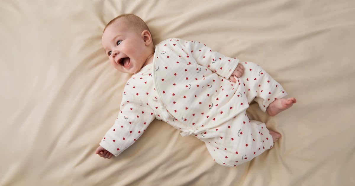 Smiling newborn baby wearing a white kimono outfit with red hearts on beige fabric
