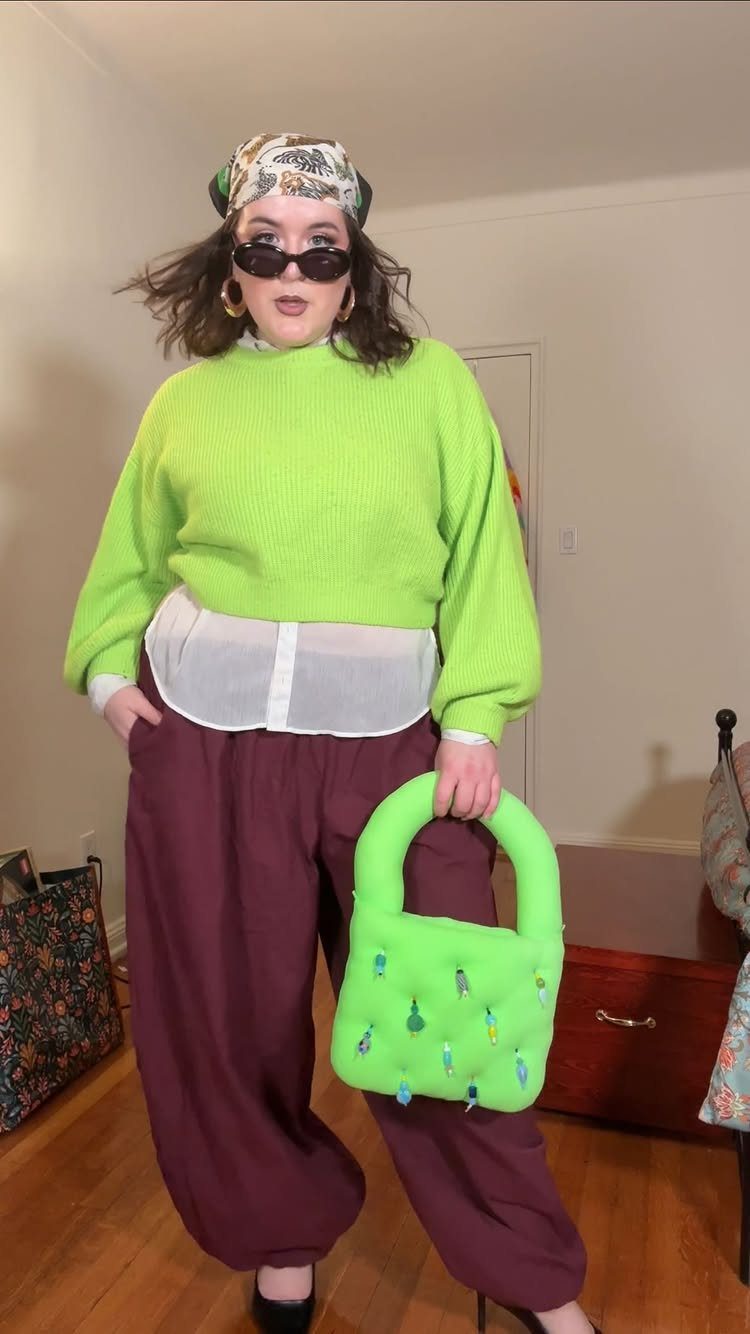 Plus-size woman in lime green sweater and maroon trousers posing with a green handbag.