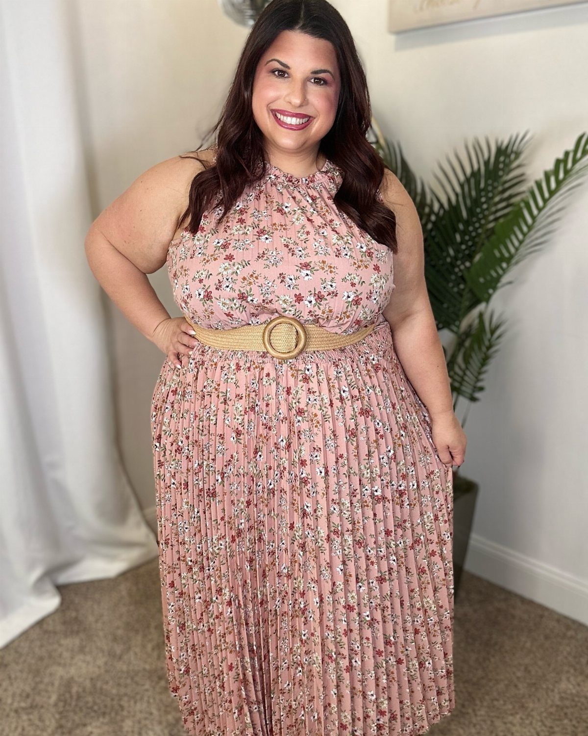 Plus-size woman wearing a pink floral pleated maxi dress with a woven belt.