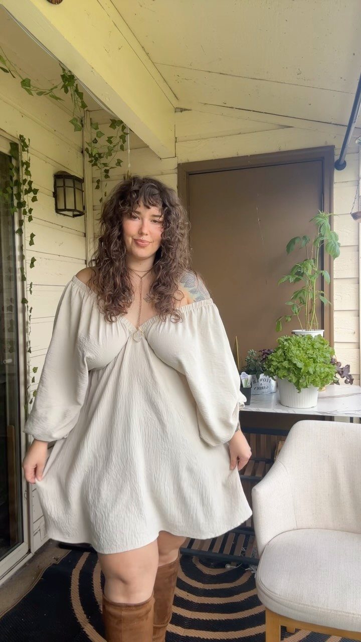 Plus-size woman wearing a chic cream off-the-shoulder dress and brown boots on a porch.