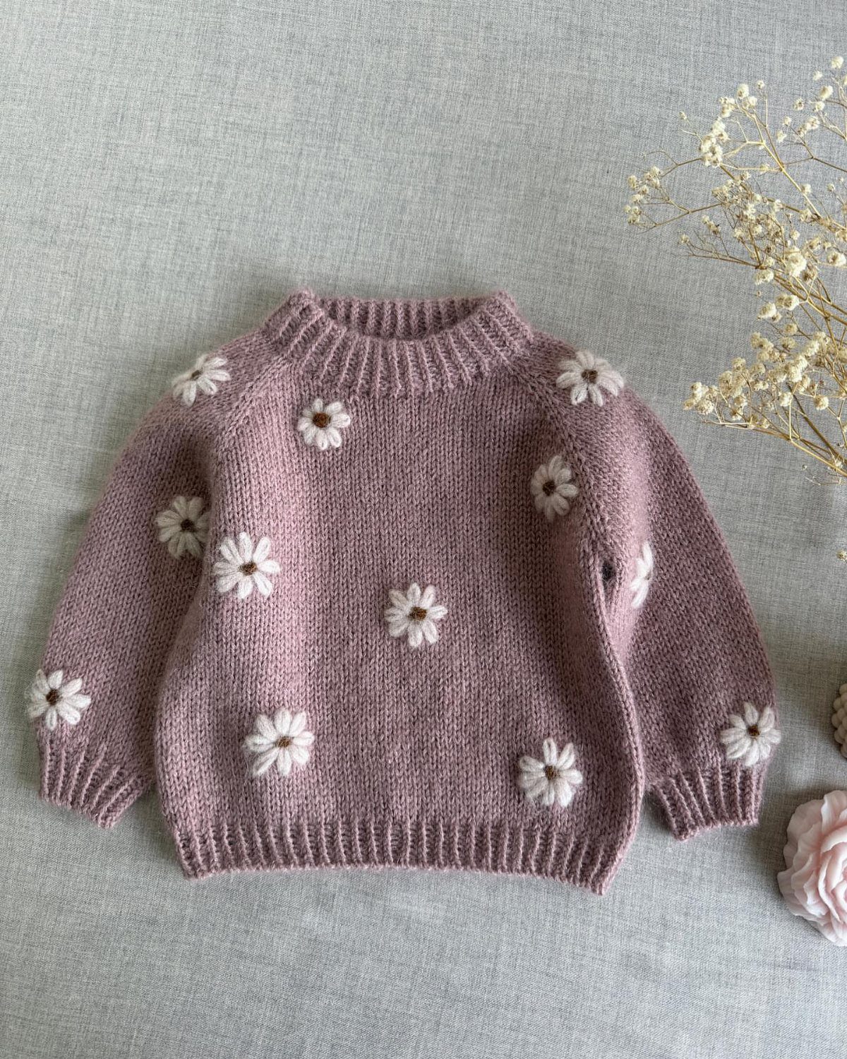 Chinese Infant Clothing: 7 Ideas for Baby Outfits 1 Mauve knitted baby sweater with white daisy flowers on a grey background