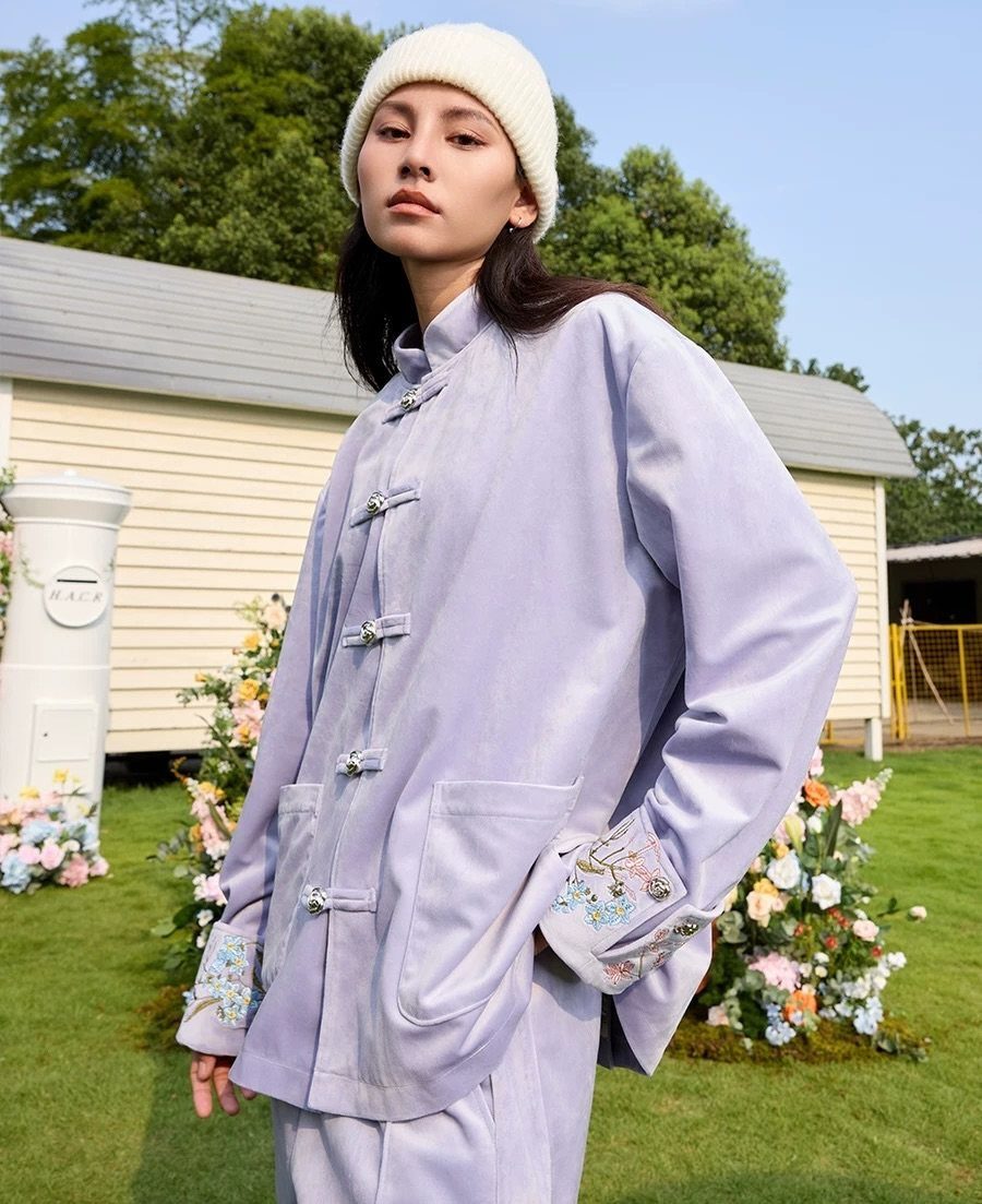 Woman wearing a light purple Chinese-inspired jacket with frog closures and embroidered cuffs.