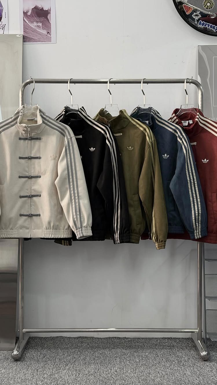 Cream athletic jacket with Chinese frog buttons hanging on a metal clothing rack.