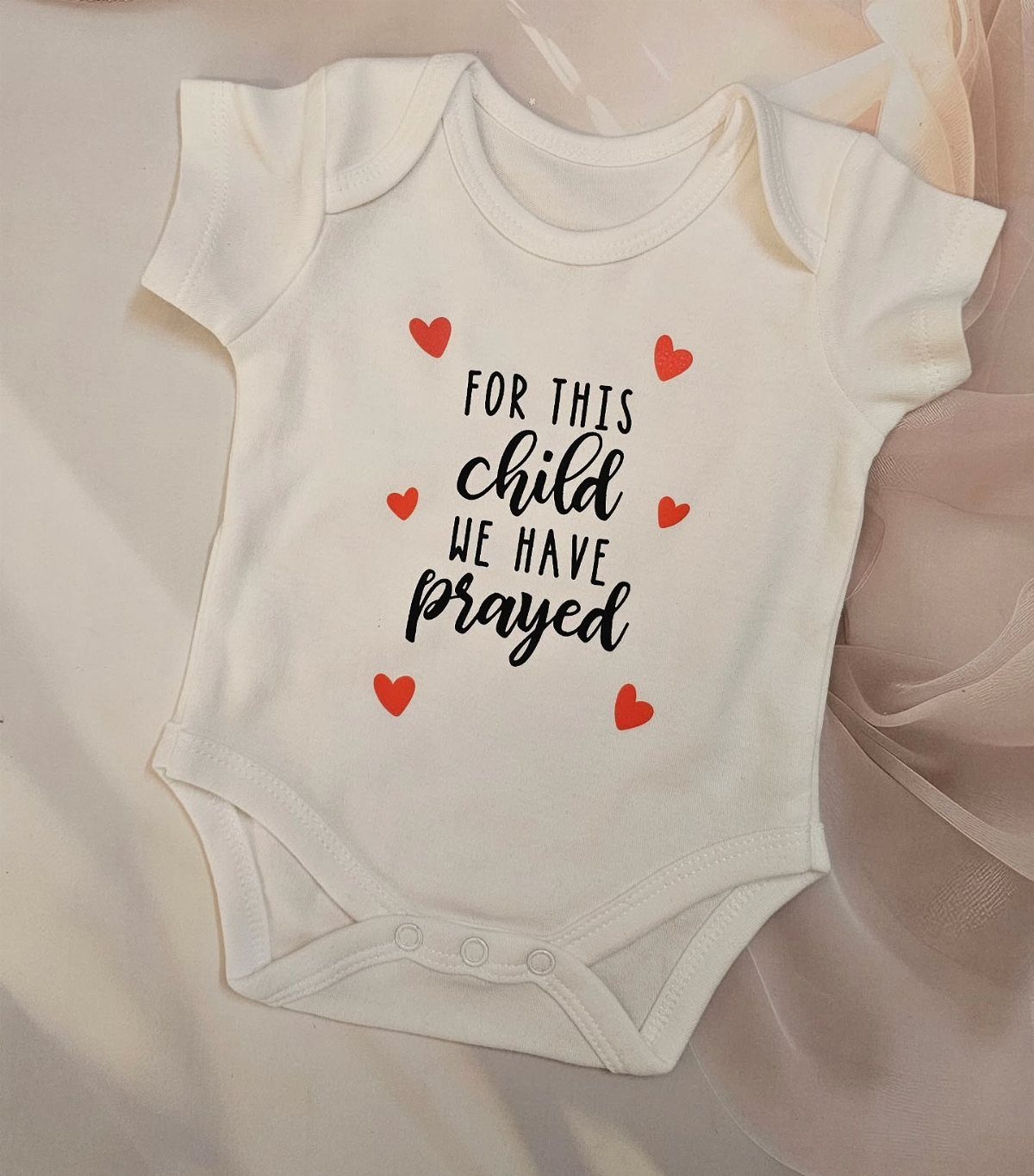 Christian Newborn Clothes for Baptism and Beyond: 5 Ideas 2 White newborn onesie with the text For this child we have prayed and hearts.