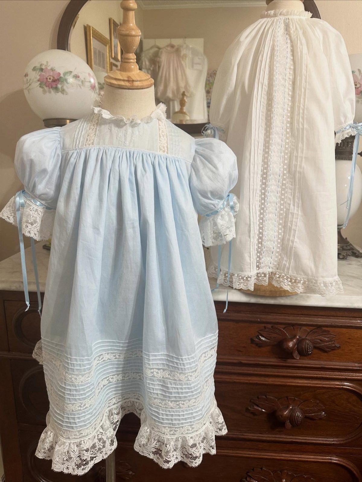 Christian Newborn Clothes for Baptism and Beyond: 5 Ideas 3 Light blue and white lace newborn gowns displayed on mannequins atop a dresser.