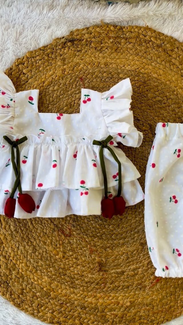 White baby outfit with cherry print and ruffles on a woven jute mat