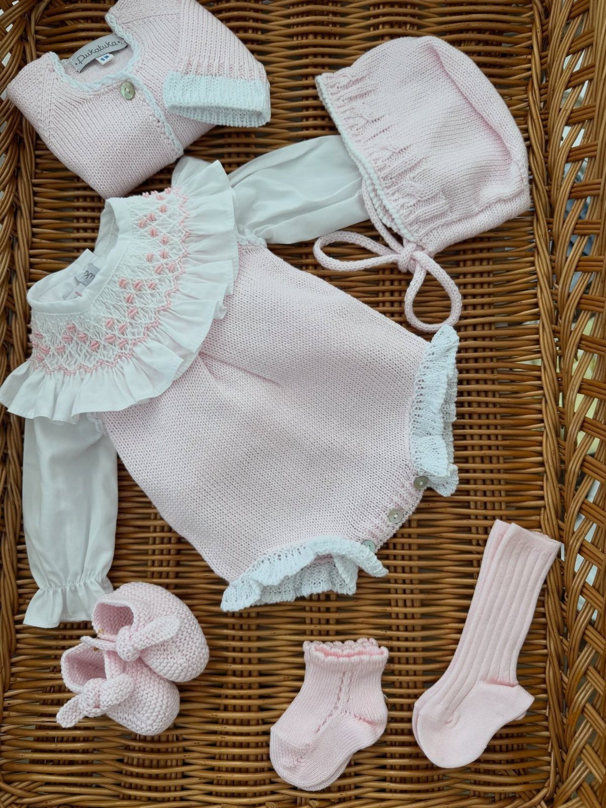 Pink and white knitted baby dress set with bonnet and booties in wicker basket