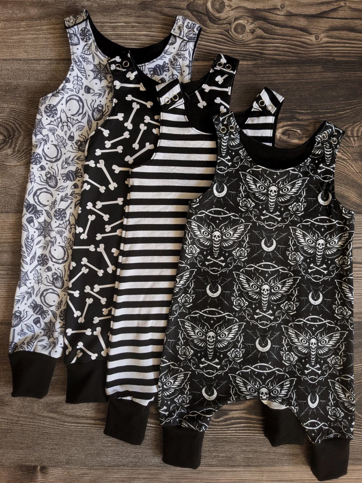Edgy Infant Clothing Ideas: 6 Looks from Skater to Goth 3 Four black and white infant jumpsuits with edgy gothic and skeletal patterns on wood.