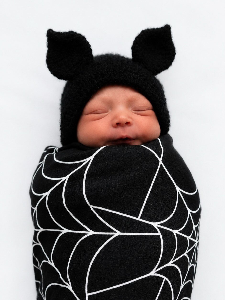 Edgy Infant Clothing Ideas: 6 Looks from Skater to Goth 5 Newborn baby in a black spiderweb swaddle and black knitted ear hat.
