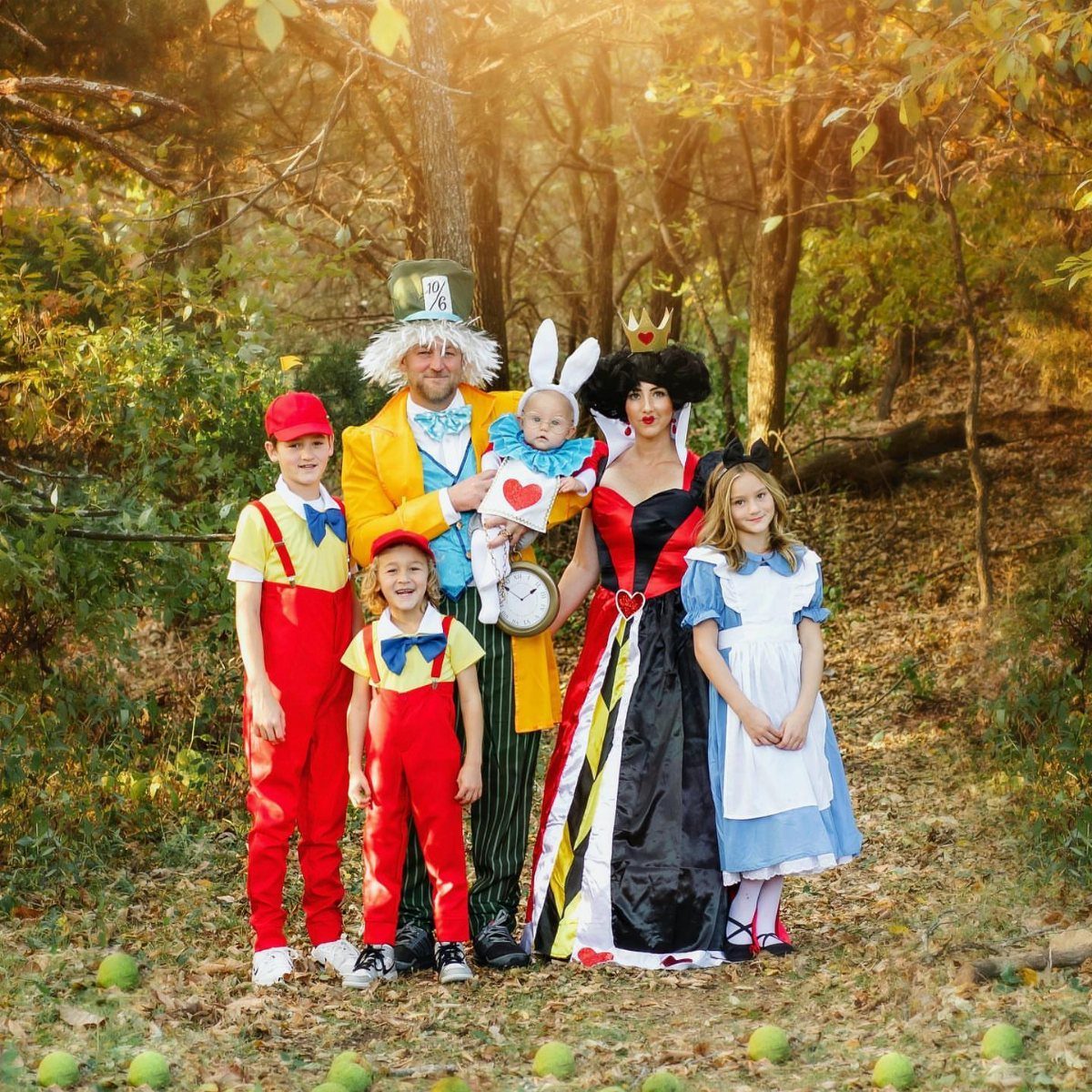 Family in Alice in Wonderland costumes posing in a forest with a newborn baby.