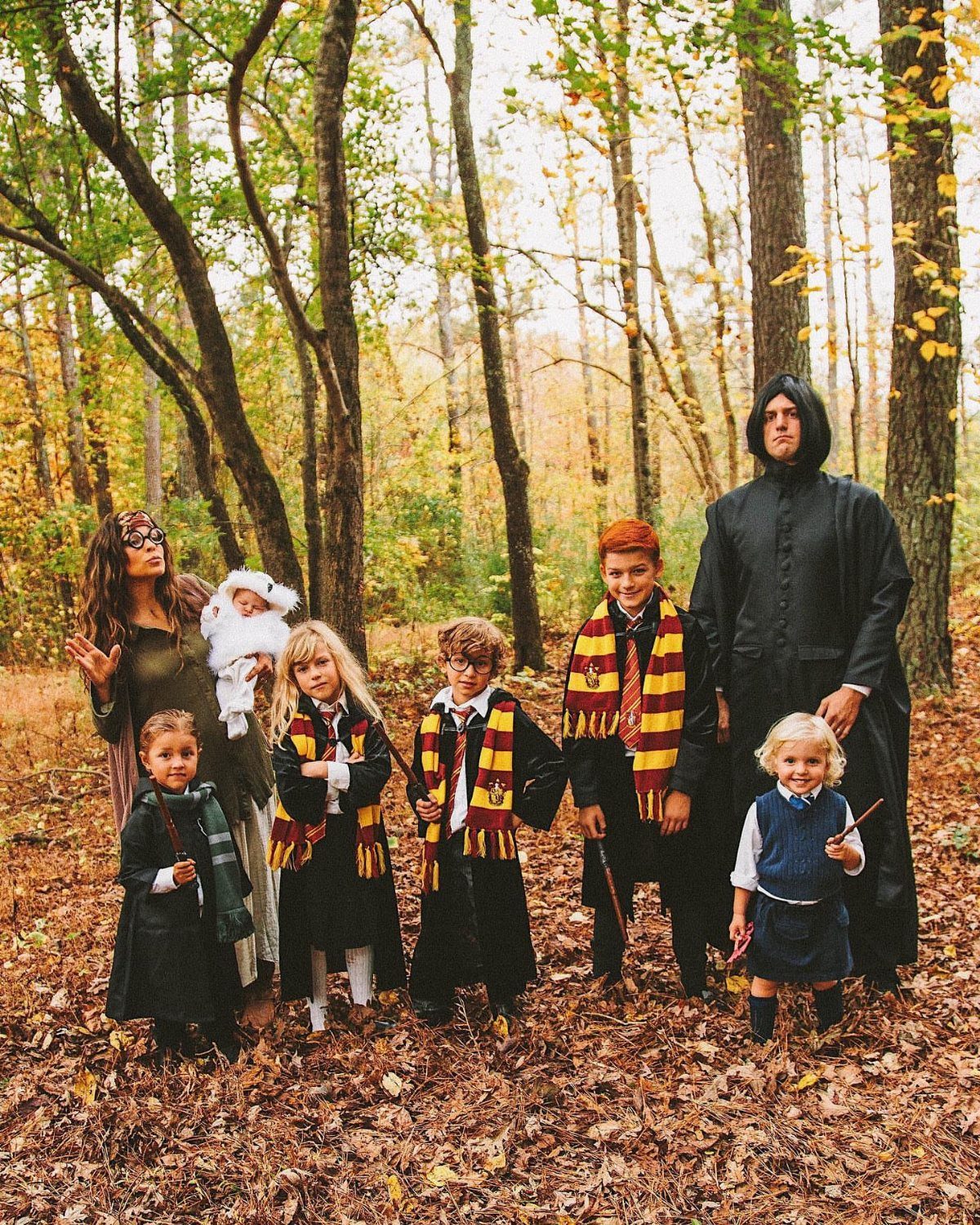 Family in Harry Potter costumes posing in an autumn forest with a newborn baby.