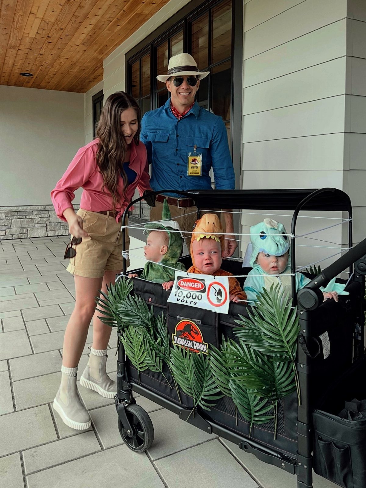 Family in safari outfits with three babies dressed as dinosaurs in a decorated wagon.