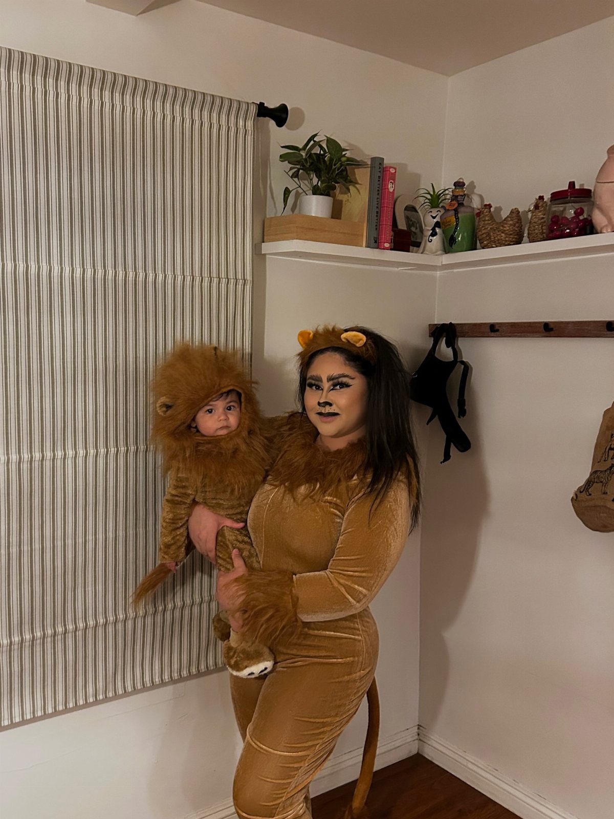 Woman and baby wearing matching brown lion costumes posing indoors against a wall.