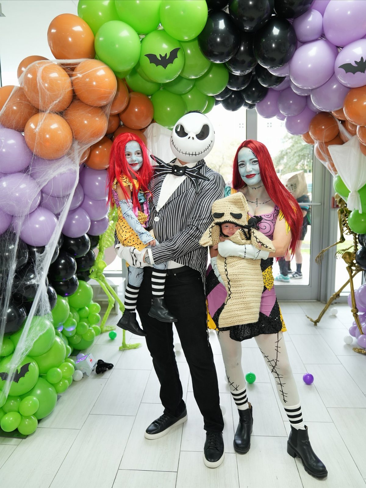 Family dressed as characters from The Nightmare Before Christmas posing by balloon arch.