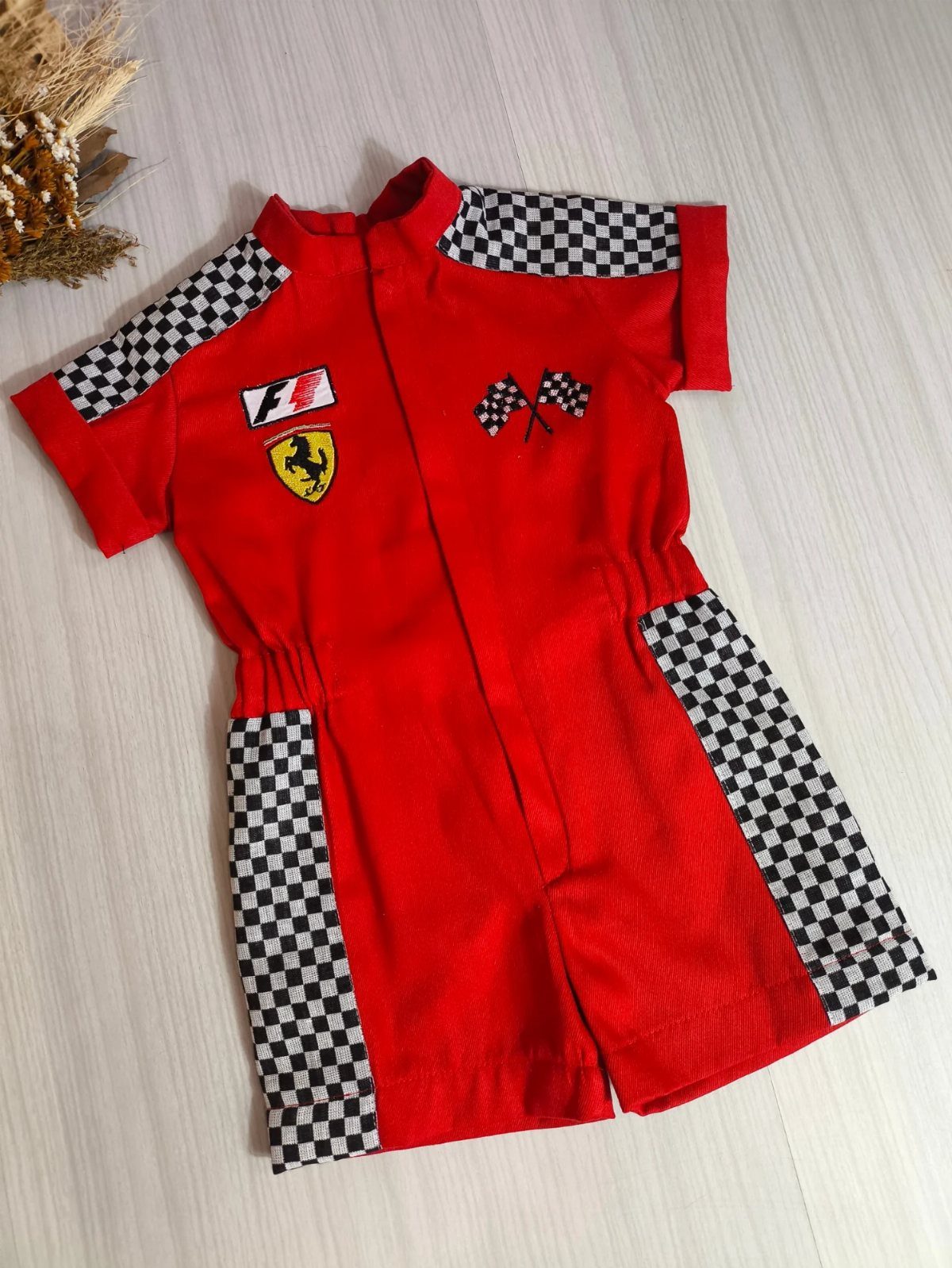 Ferrari Newborn Clothes: 8 Ideas for Red Racing Looks 7 Red Ferrari baby jumpsuit with checkered patterns and logo on light wood background