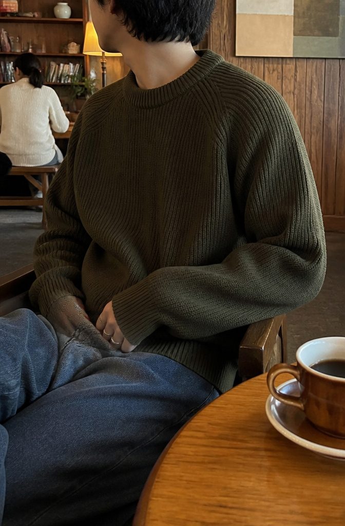 A young man sitting in a café wearing a casual sweater.