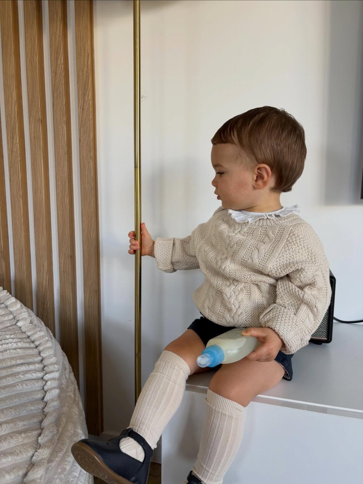 Toddler wearing a cream cable-knit sweater with a white collar and knee-high socks.