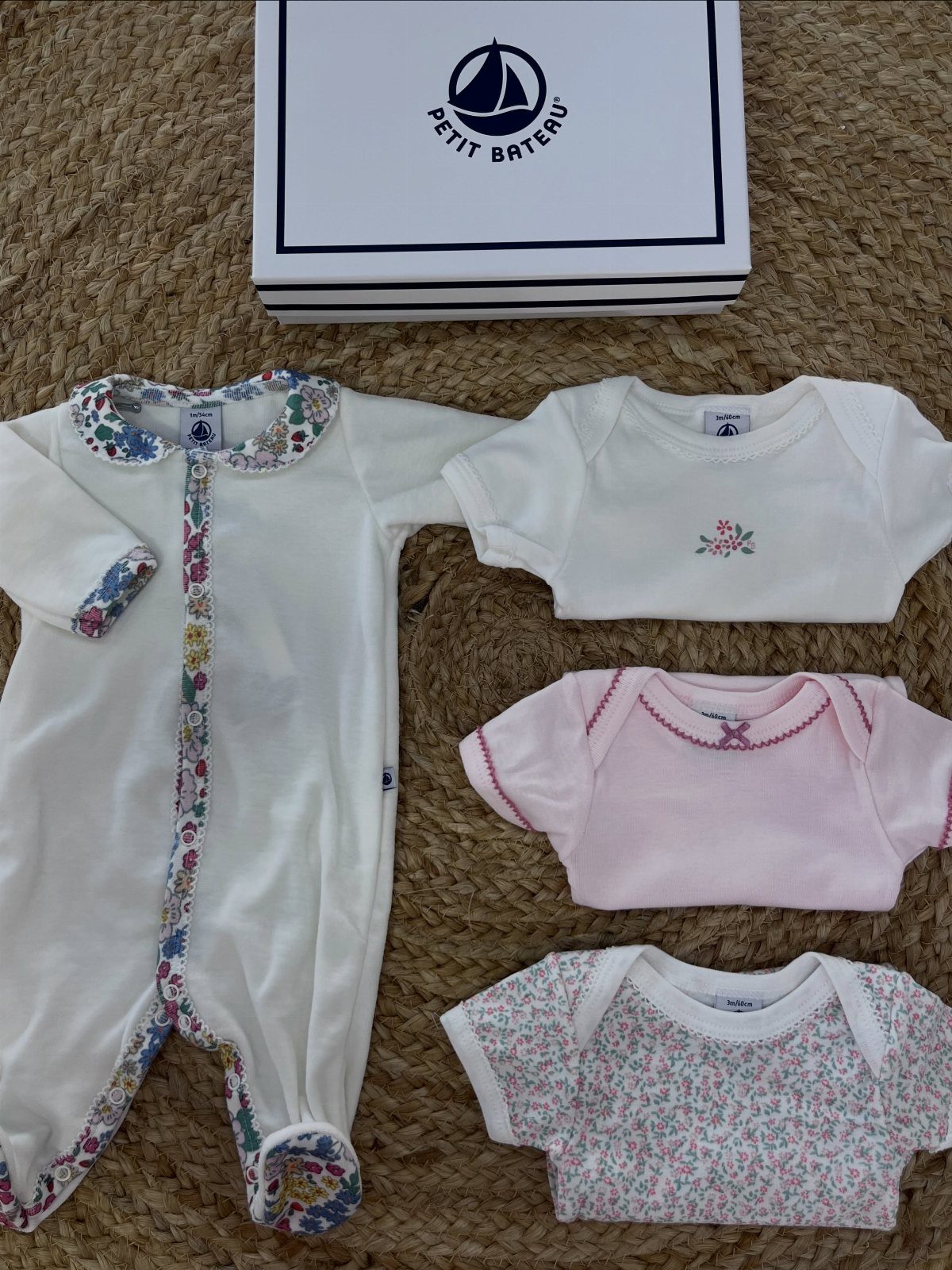 Baby sleeper and bodysuits in white and pink laid next to a branded box.