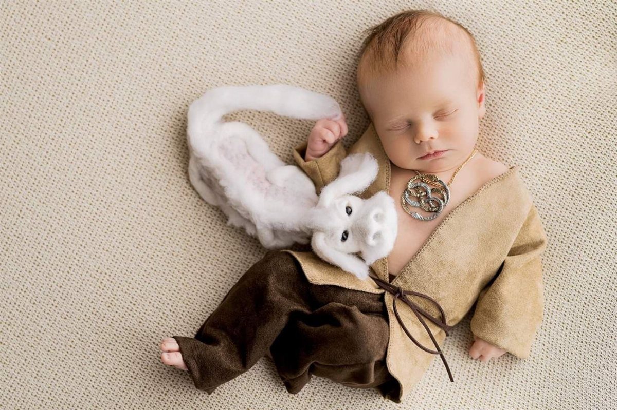 Sleeping newborn baby in tan tunic and brown pants with a white plush dragon
