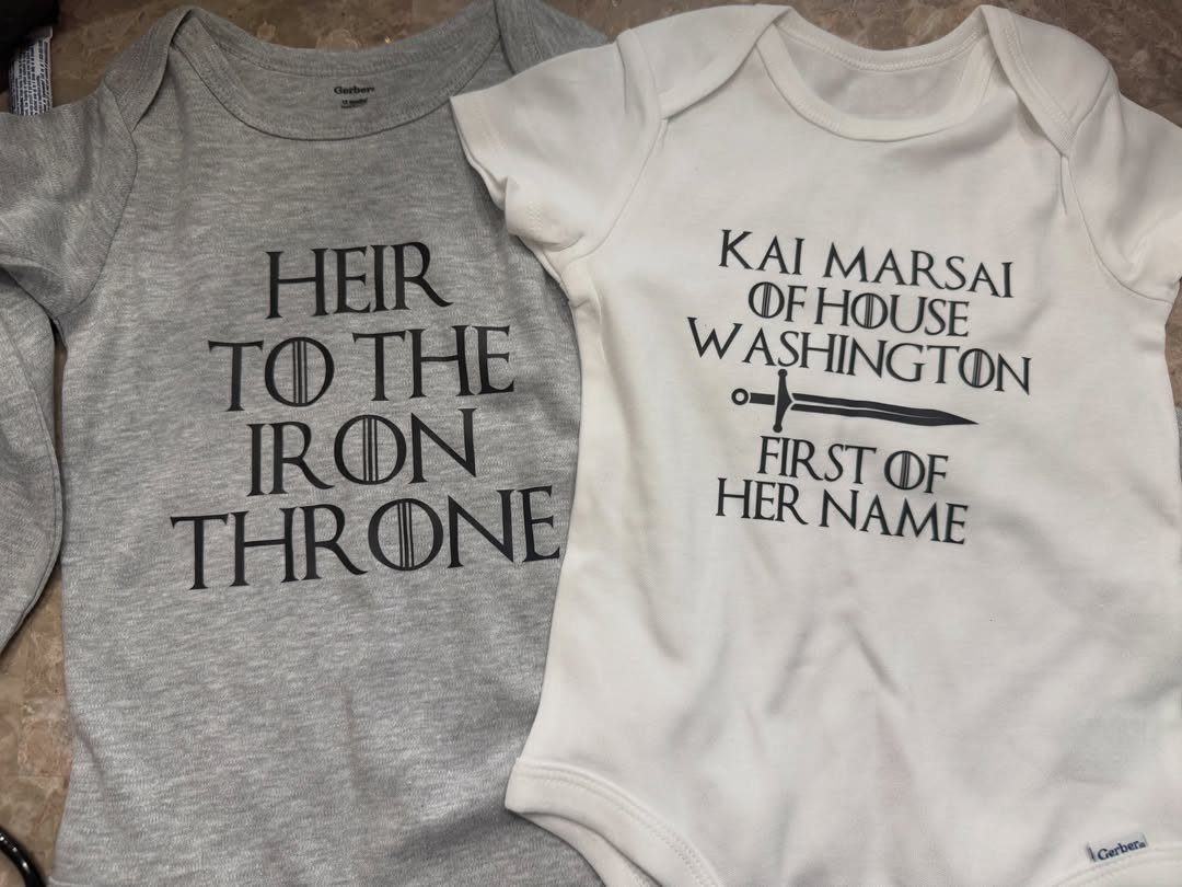 Two baby onesies with Game of Thrones themed text in black ink.