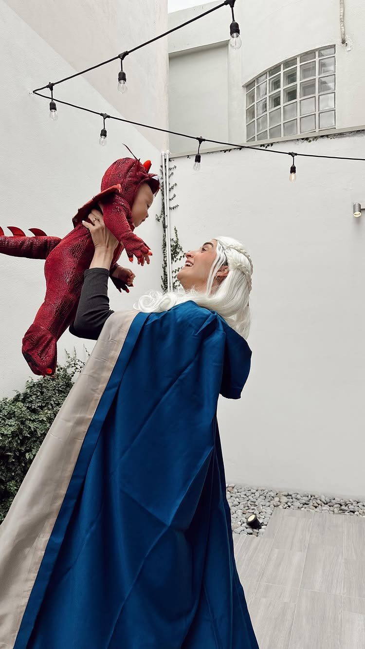 Woman in Daenerys costume holding a baby wearing a red dragon outfit outdoors.