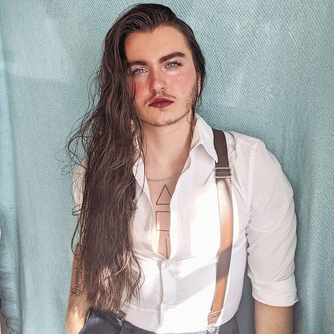 15 Gender Neutral Clothing Ideas for Everyday Style 9 Person with long hair wearing a white button-up shirt and brown suspenders.