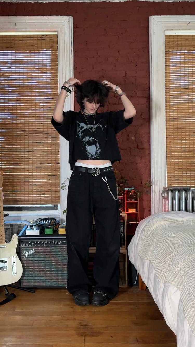 15 Gender Neutral Clothing Ideas for Everyday Style 13 Person wearing a black cropped graphic tee and wide-leg black trousers in a room.