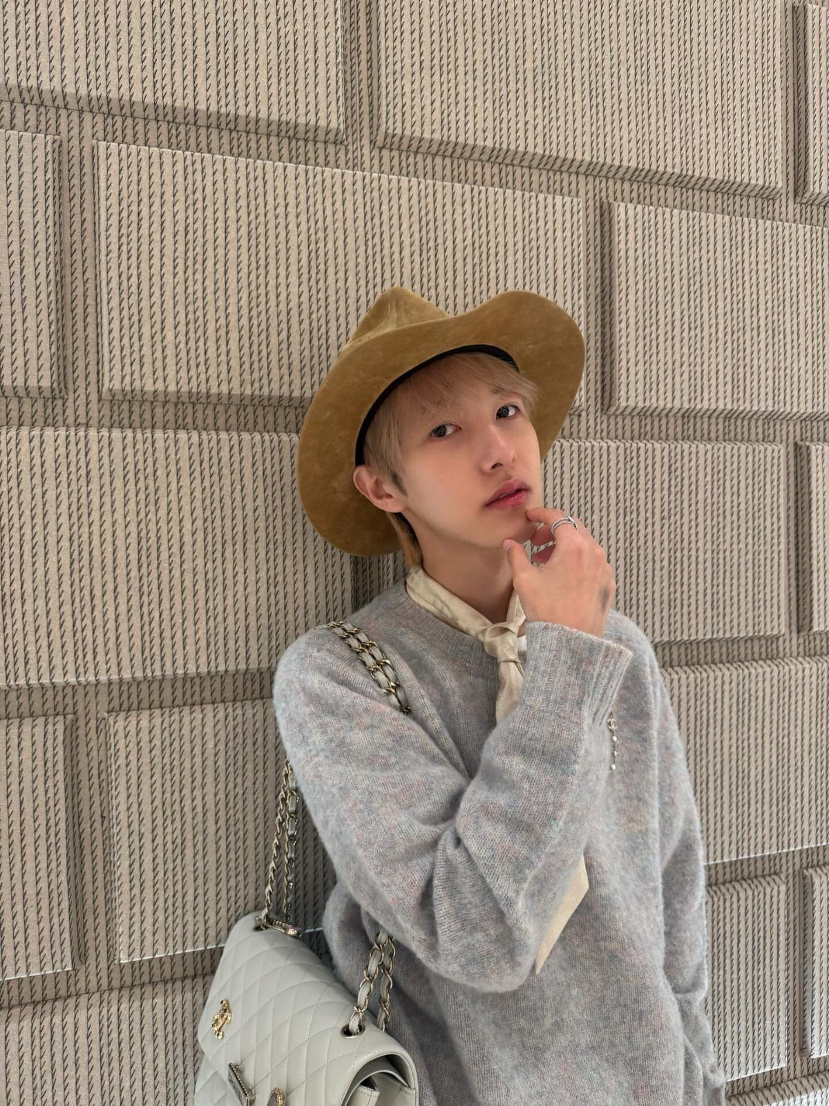 15 Gender Neutral Clothing Ideas for Everyday Style 2 Person wearing a brown hat and white quilted handbag against a textured wall