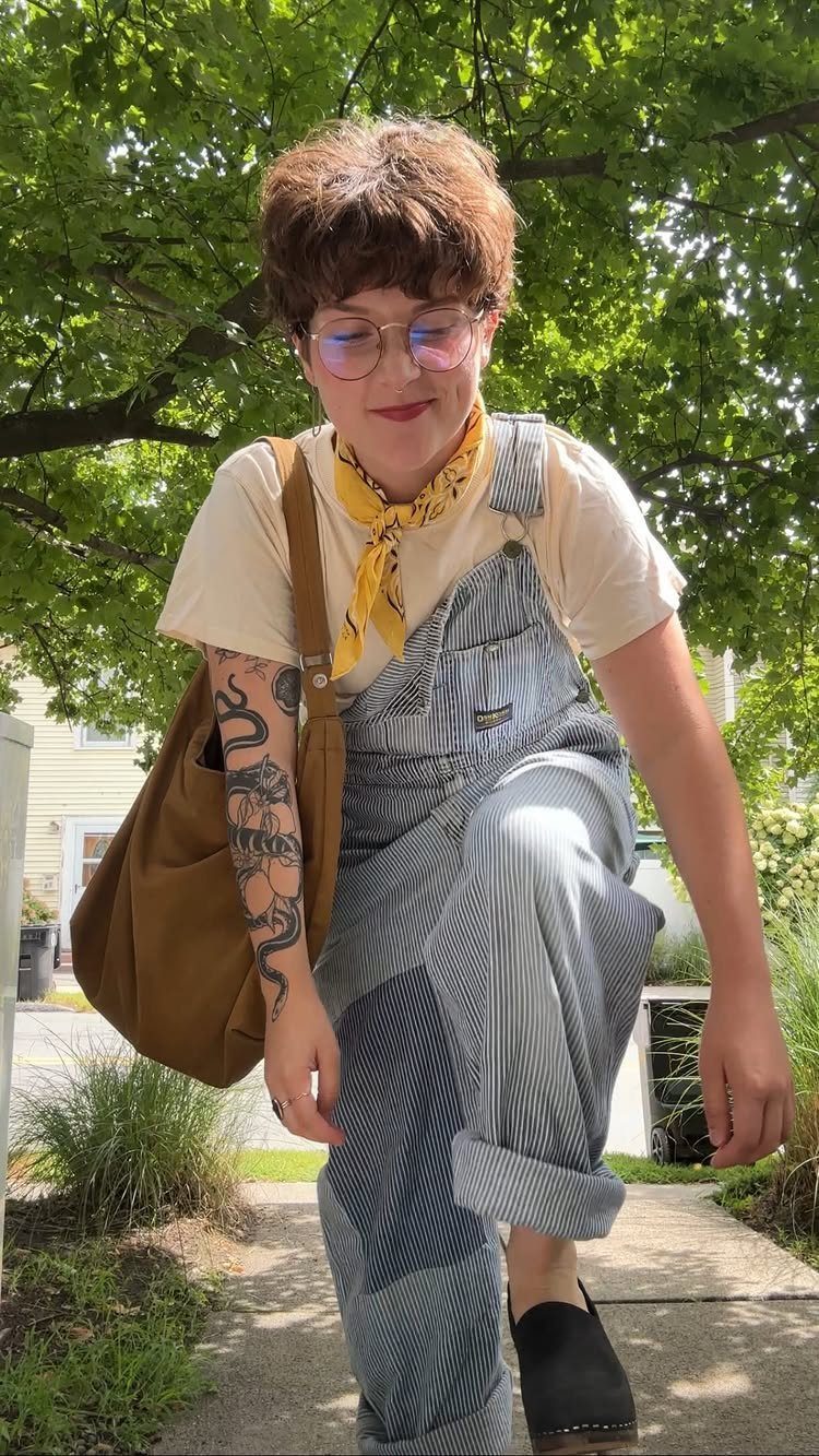 15 Gender Neutral Clothing Ideas for Everyday Style 6 Person wearing striped overalls, a cream t-shirt, and yellow neckerchief outdoors.