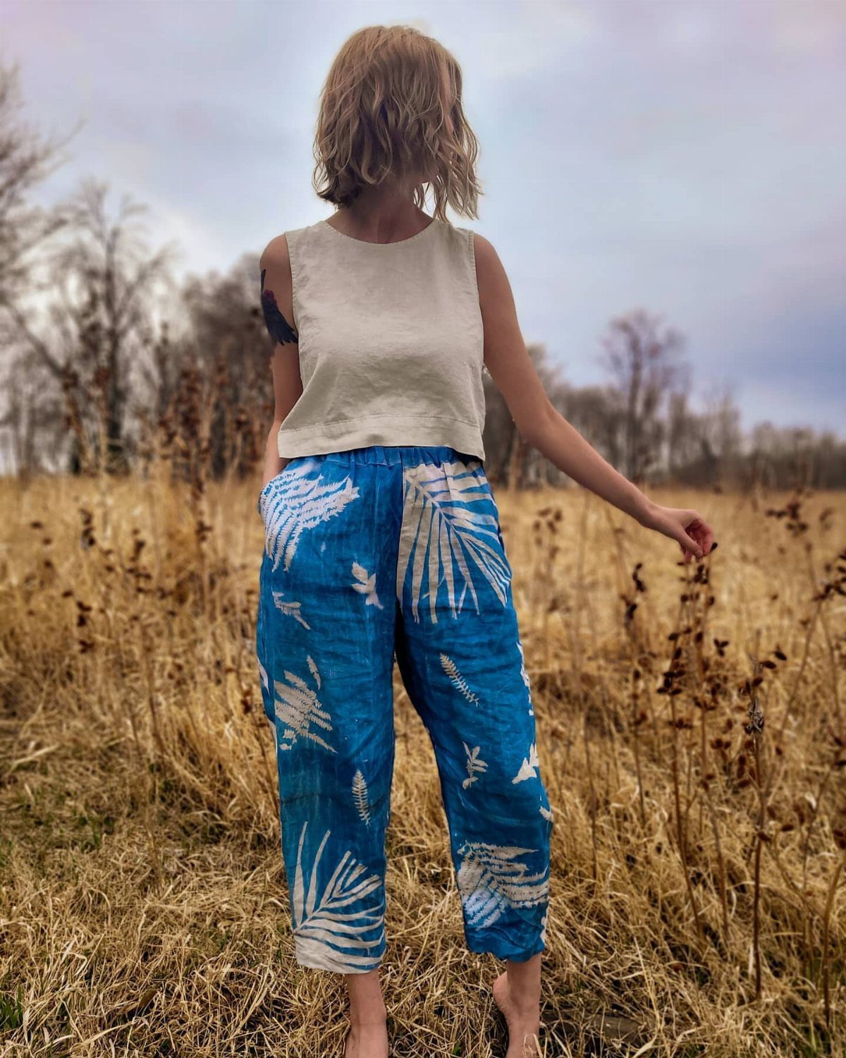 15 Gender Neutral Clothing Ideas for Everyday Style 8 Person in a cream top and blue leaf-patterned pants standing in dry grass.