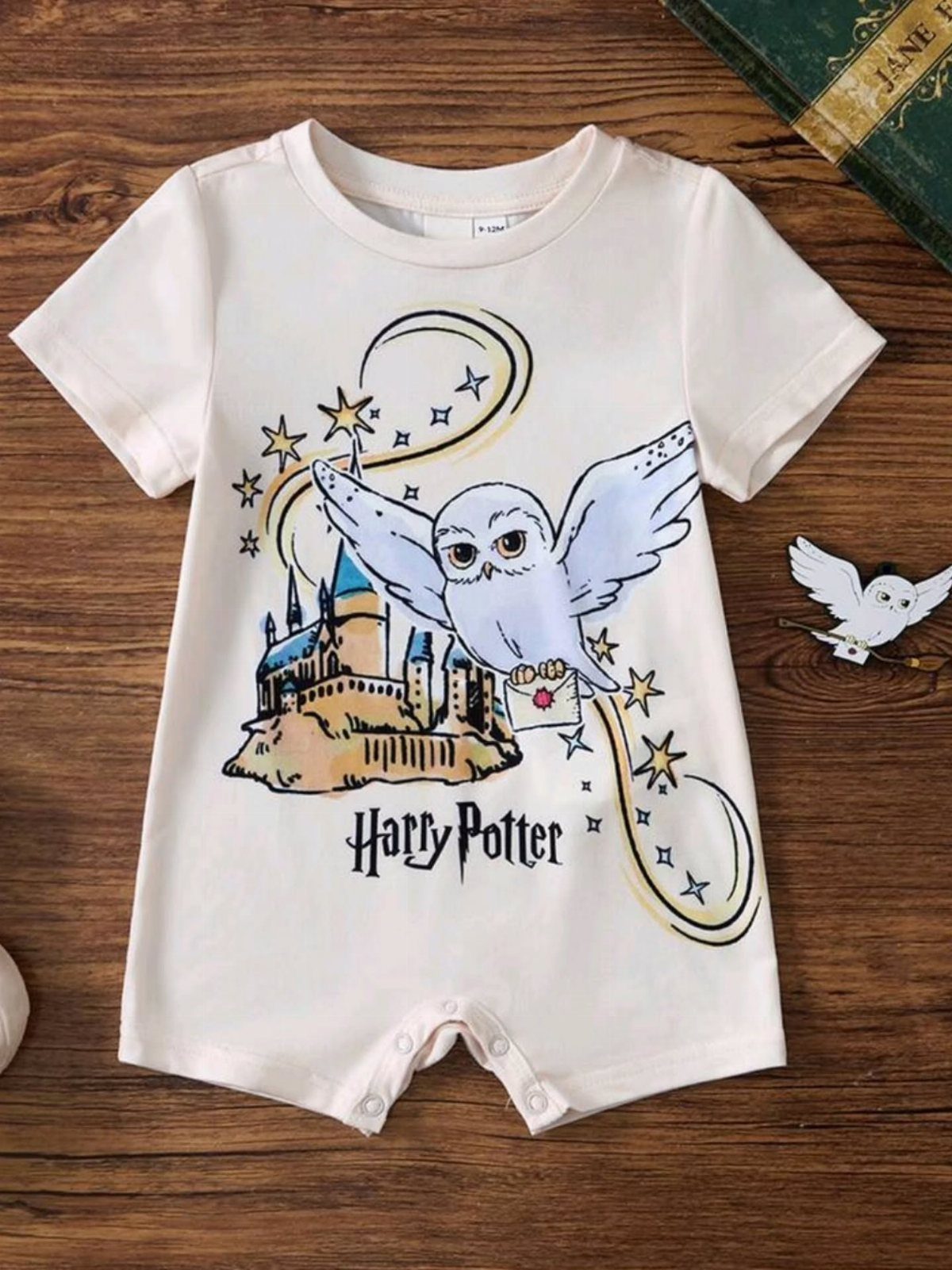 Harry Potter Baby Clothes: 5 Ideas for Little Wizards 2 White baby romper featuring Hedwig the owl and Hogwarts castle on wooden background