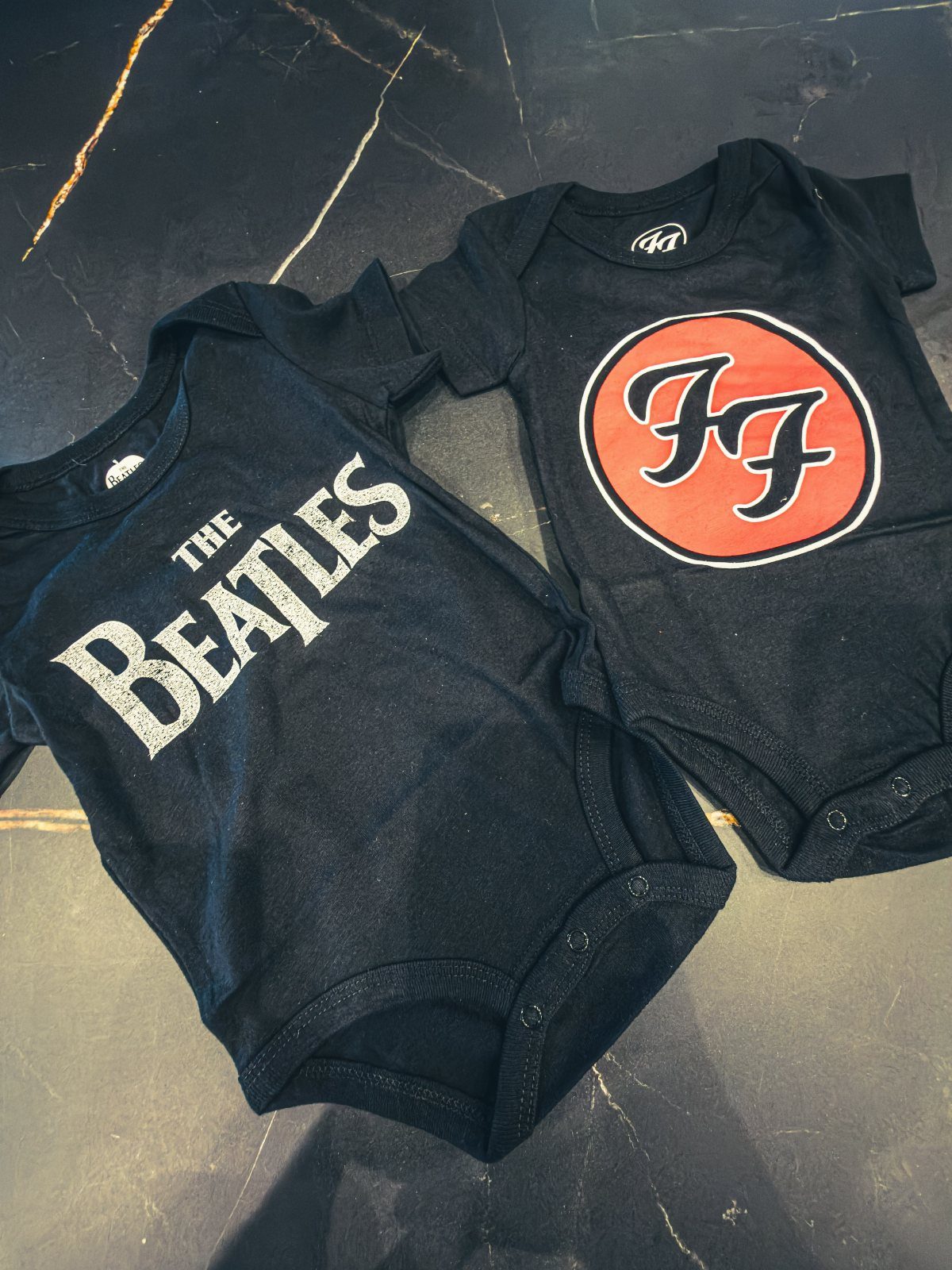 Infant Beatles Clothing: 3 Ideas for Onesies, Bibs and More 2 Two black infant bodysuits with Beatles and FF logos on a dark surface.
