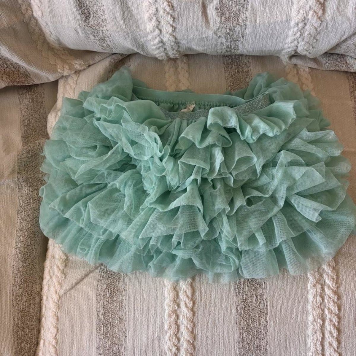 Infant St Patty's Day Clothing: 7 Ideas for Baby 1 Sage green ruffled tulle bloomers resting on a striped beige fabric surface.