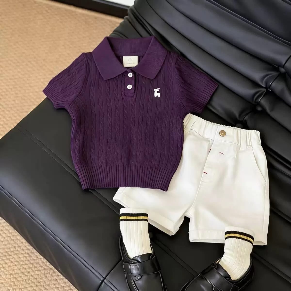 Purple polo shirt and white shorts with loafers laid on black leather.