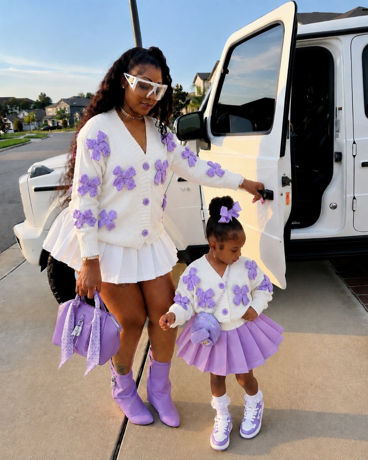 Woman and young girl in matching white and purple outfits by a white car.