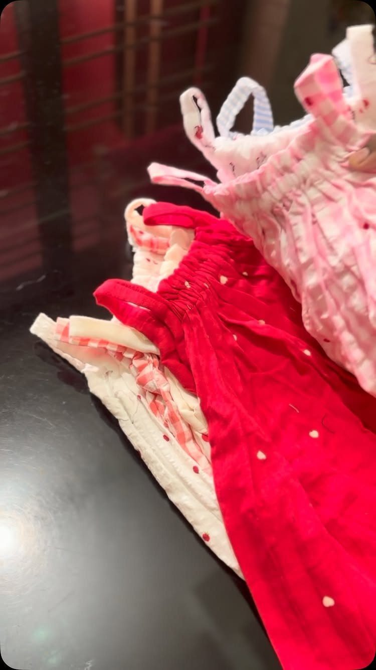 Three small children's dresses in red, pink, and white on a dark surface.