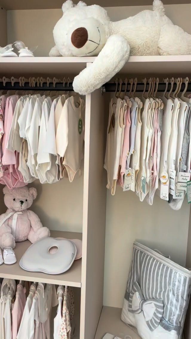Baby bodysuits in neutral tones hanging in a white wardrobe with teddy bears.