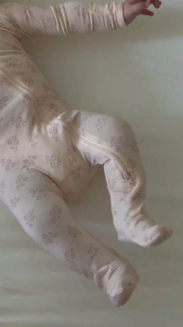 Baby wearing beige floral footed pajamas lying on a white background