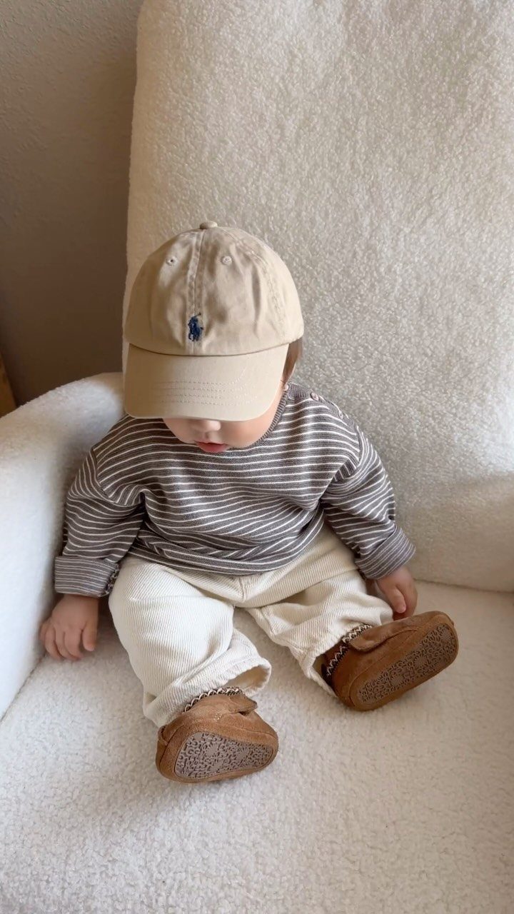Baby wearing a striped shirt and off-white corduroy pants sitting in a chair