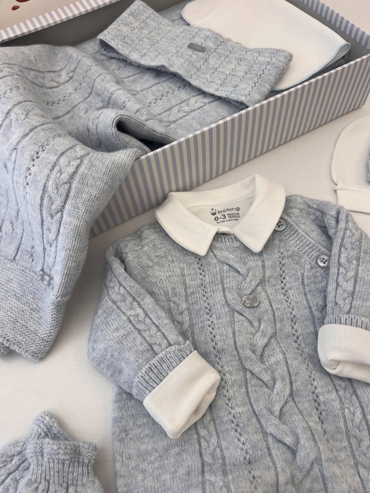 Grey cable-knit newborn sleepsuit and hat arranged in a striped gift box.