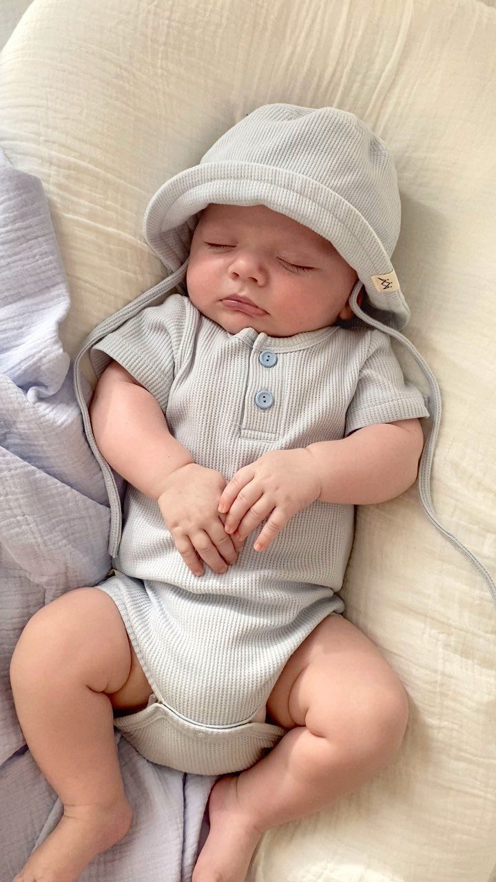 Sleeping newborn baby wearing a light grey ribbed bodysuit and matching bucket hat.