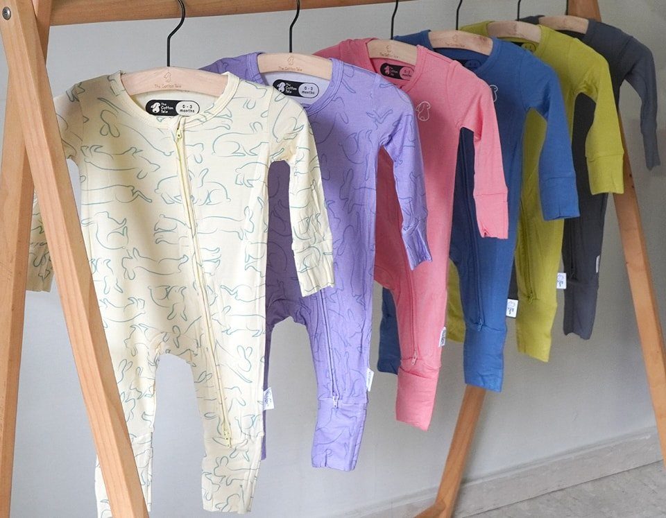 Newborn Clothes Made in USA: 3 Ideas for Gifts and Daily Wear 2 Colorful long-sleeve baby rompers hanging on a light wooden clothing rack.